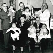 Civic leaders pose with babies to promote the giving out of free orange juice and cod liver oil