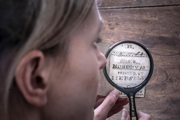 Keighley News: Curator Sarah Laycock uses a magnifying glass to inspect the manuscript. Picture: PA